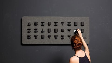 Anerkennung Nachwuchs – alphabetum tactus Frau vor einer schwarzen Tafel mit erhobenen Buchstaben.