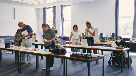 Mehrere Jurymitglieder betrachten sich die Einreichungsexponate auf Tischen